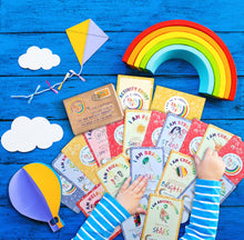 Load image into Gallery viewer, A collection of colorful children&#39;s affirmation cards displayed on a blue wooden surface, accompanied by illustrated images such as a rainbow, kite, and clouds, indicative of a fun and supportive learning activity.
